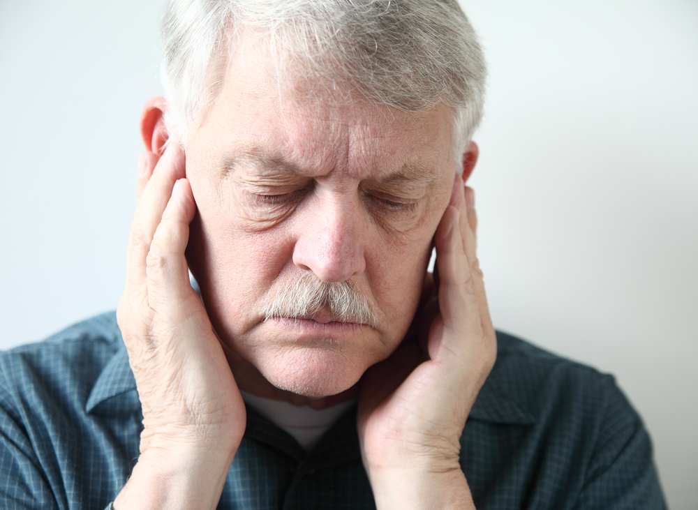 older man holds both hands to his upper jaw near the ears stock photo