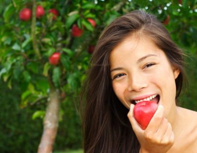 happy smiling young beautiful woman eating red apple stock photo