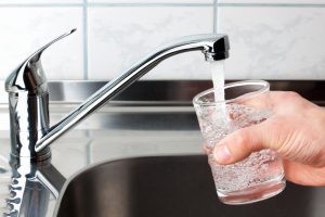 Hand holding a glass of water poured from the kitchen faucet stock photo