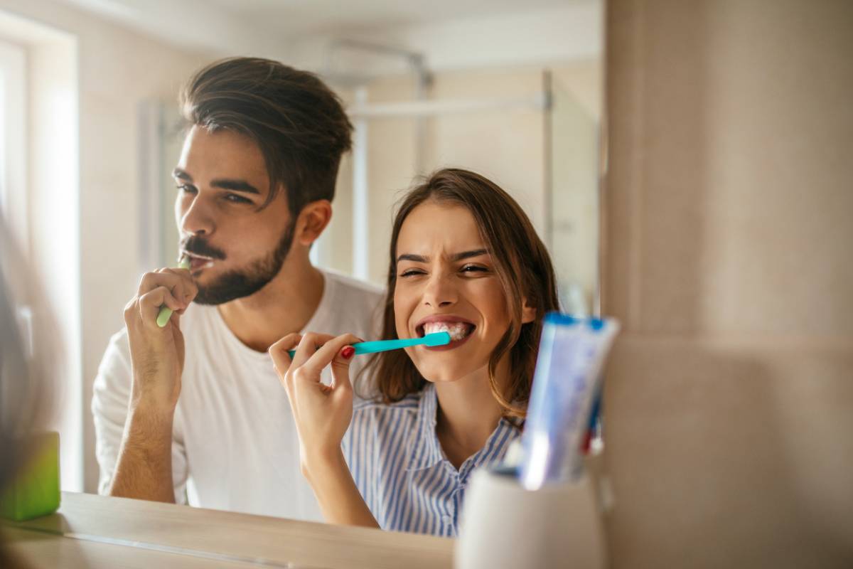 happy couple bonding while brushing teeth in the bathroom stock photo